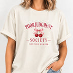 Woman wearing the Poor Judgment Society Lifetime Member tee in Ivory with deep red lettering