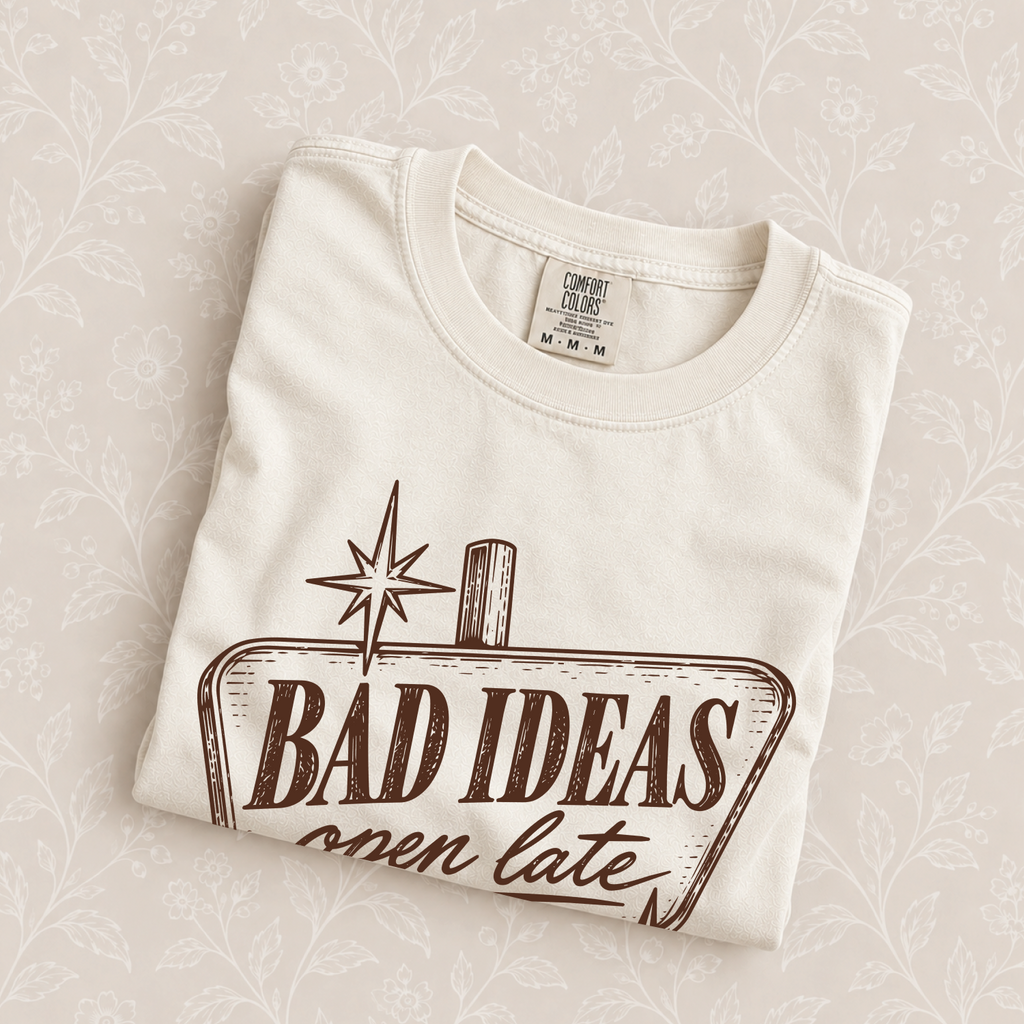 Bad Ideas, Open Late tee in Ivory folded on a cream floral surface, sign close up
