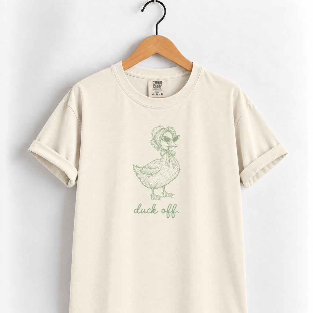 Duck Off tee in Ivory on a wooden hanger, sage green duck design center chest