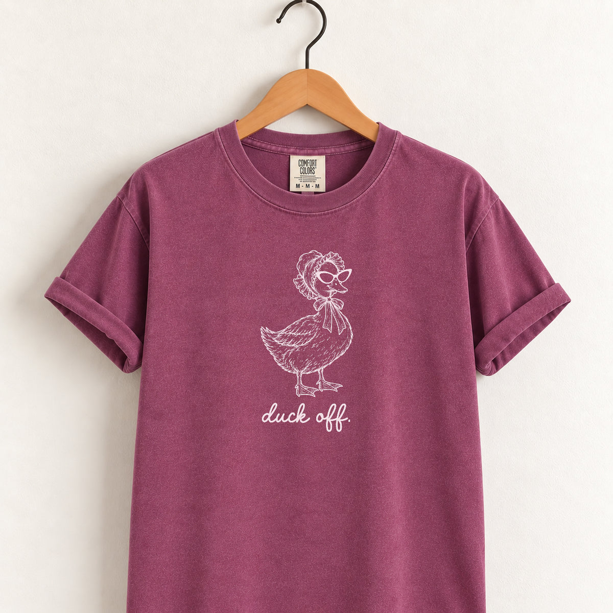 Duck Off tee in Berry on a wooden hanger, blush duck design center chest